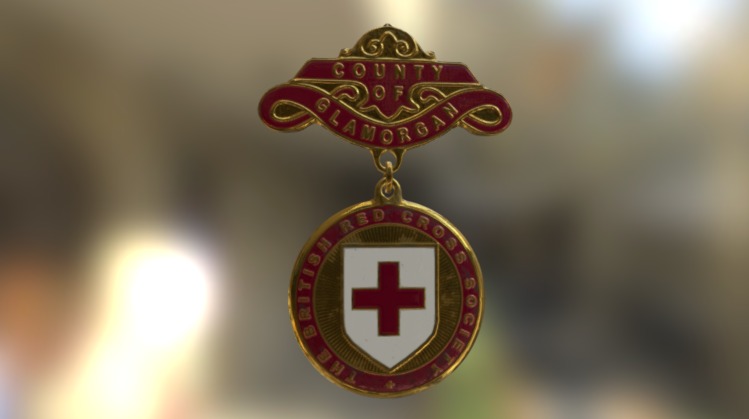 It would be pinned on the left side of the chest, it has a metal red, white and gold badge, with an upper red banner in which it is written “County of Glamorgan” and a lower encircled red cross hanging down, the circle reads “British Red Cross Society” 3d model